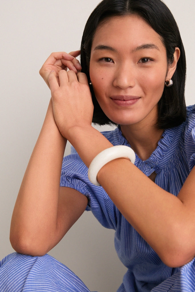 Young woman wearing a classic, light-blue pinstriped blouse showcases the Swirl Chalk Crescent Cuff, an effortless, high-end bracelet blending resin and metal for a fun, bold statement.