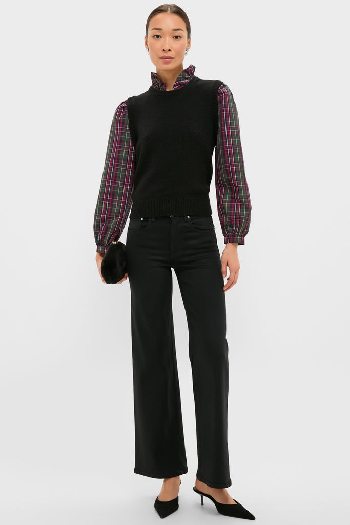 Woman wearing the Tartan Ella Sweater Blouse, a classic knit vest over a plaid ruffled blouse, paired with high-waisted trousers and chic kitten-heel mules, holding a clutch.
