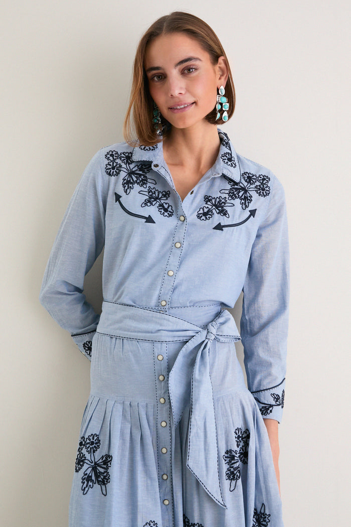 Young woman in The Chambray Embroidered Western Shirt featuring classic floral embroidery, pleated skirt, and relaxed fit, embodying effortless high-end style and fun confidence.