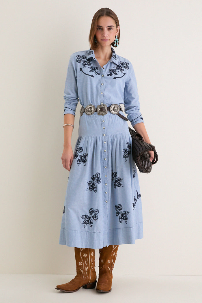 Woman in The Chambray Embroidered Western Shirt with floral embroidery, styled with a silver concho belt and cowboy boots, embodying classic, effortless, high-end fashion.