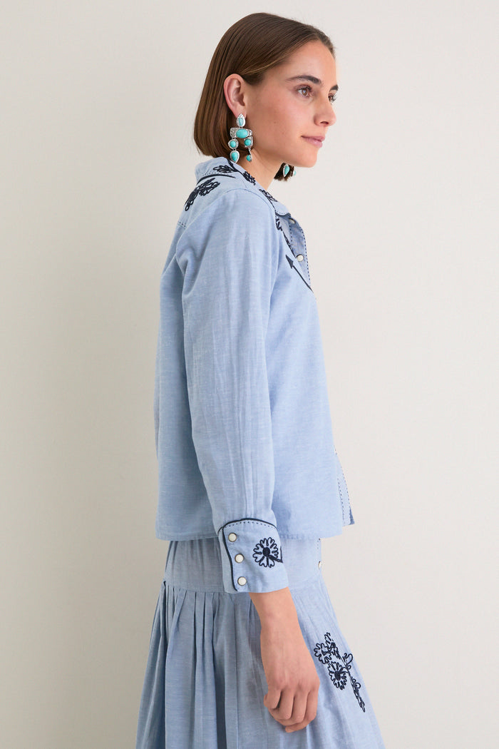 The Chambray Embroidered Western Shirt: A classic, effortless blouse with navy floral embroidery and Western pockets, styled with turquoise earrings for a fun, high-end look.