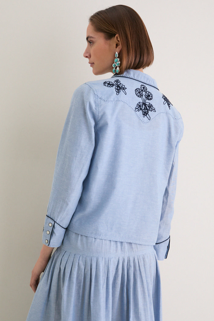 Woman in profile wearing the Chambray Embroidered Western Shirt; classic, effortless style with dark embroidery, snap-button cuffs, and a relaxed fit.