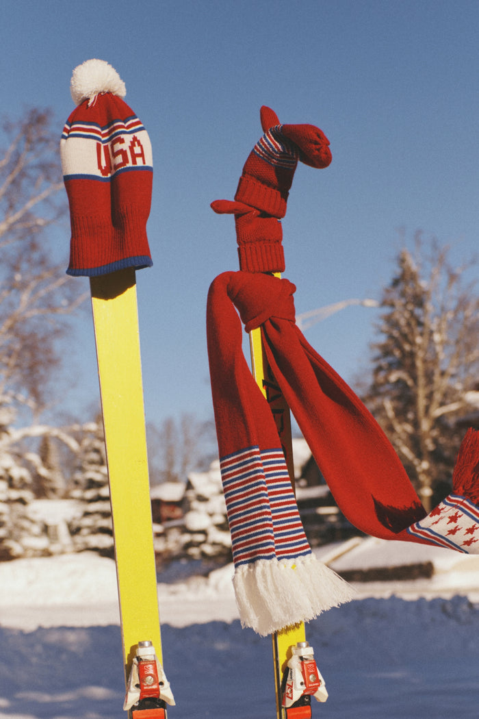 USA Telluride Hat perched on a bright yellow ski, showcasing a classic, fun, and effortless style with red winter accessories, perfect for an après-ski high-end look.