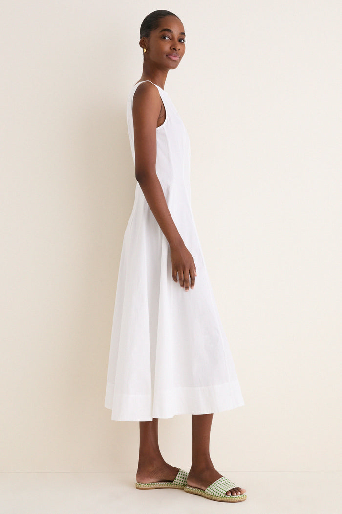 Person in profile wearing a sleeveless, ankle-length white cotton boat neck dress, exuding effortless, classic style, paired with green-and-white woven slide sandals for a fun, high-end look.