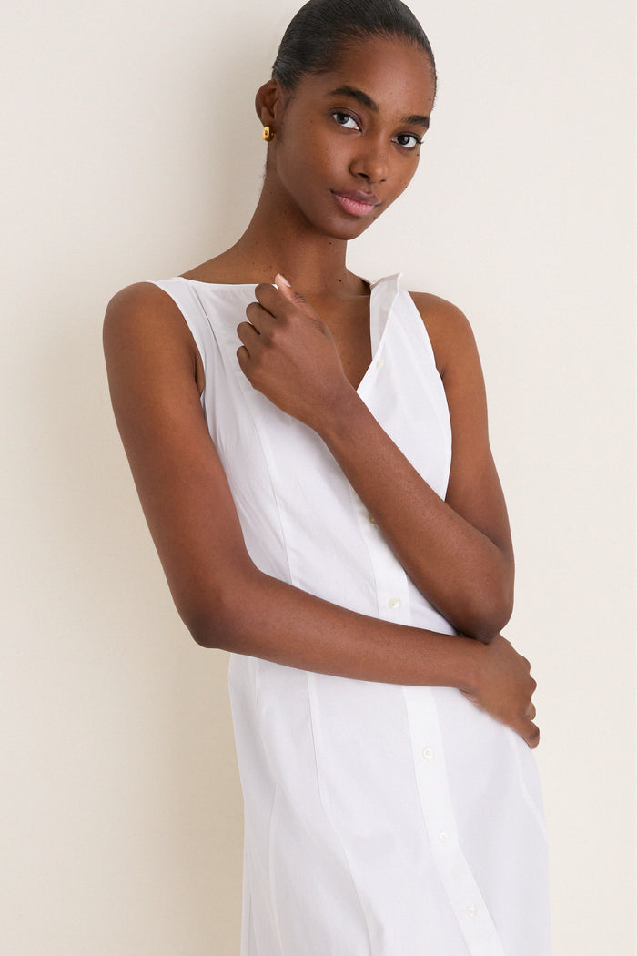 Young woman models a classic, high-end, sleeveless White Cotton Boat Neck Dress, effortlessly styled with gold hoops, embodying Tuckernuck's fun and confident fashion ethos.