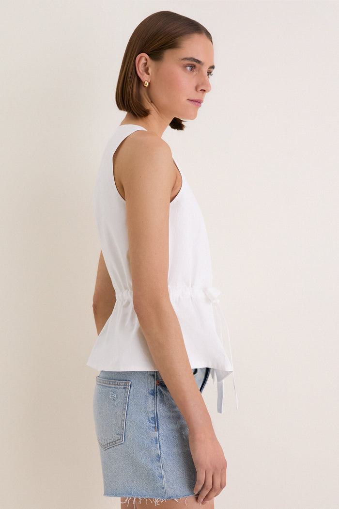 Young woman in profile wearing the White Cotton Poplin Francoise Top, featuring a high neckline and cinched waist; paired with a denim mini-skirt for classic, effortless style.