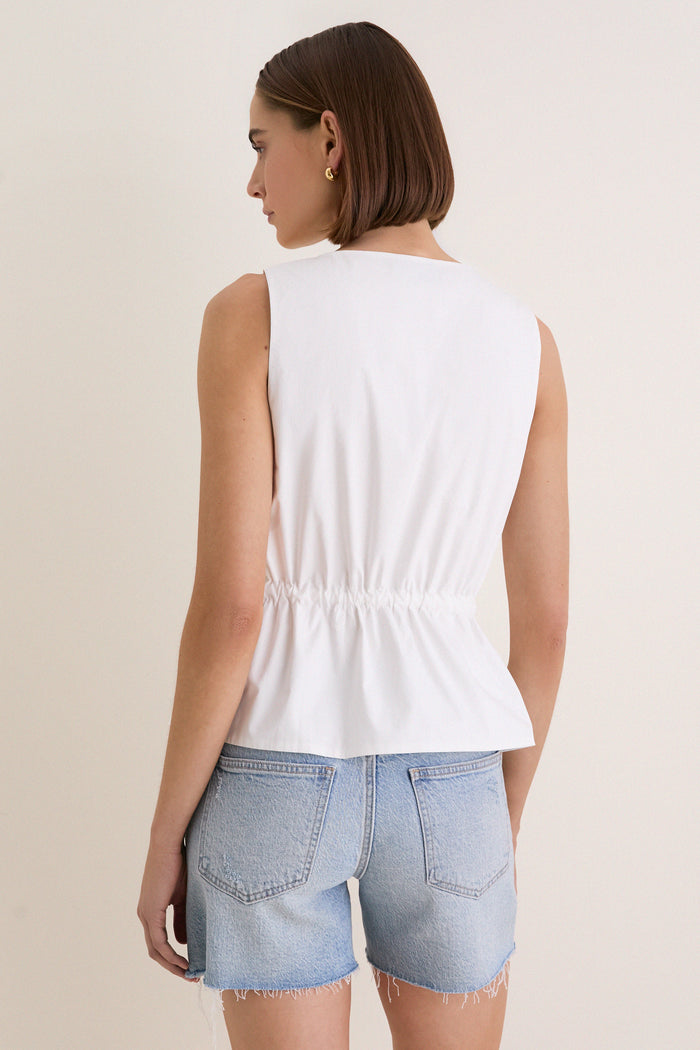 Woman wearing the classic White Cotton Poplin Francoise Top, featuring a chic high neckline, cinched waist, and fabric-covered buttons, paired with cut-off shorts for an effortless, fun look.