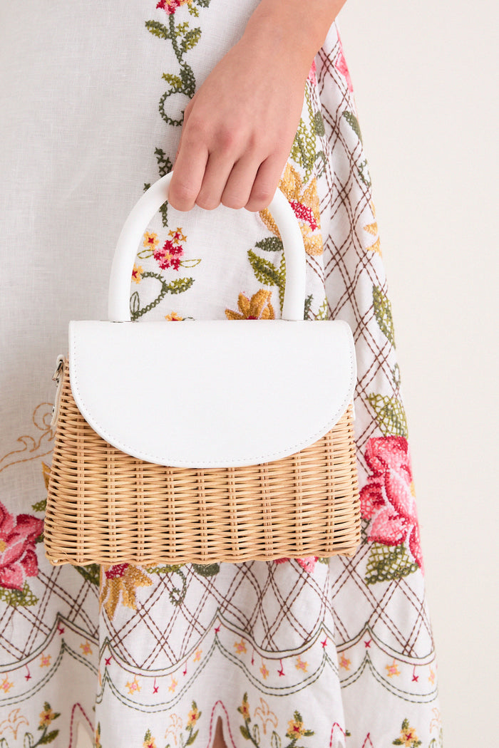 White Elle Wicker Top Handle bag, featuring a classic wicker body and sleek vegan leather trim, effortlessly held by a hand, exuding high-end and fun summer style.