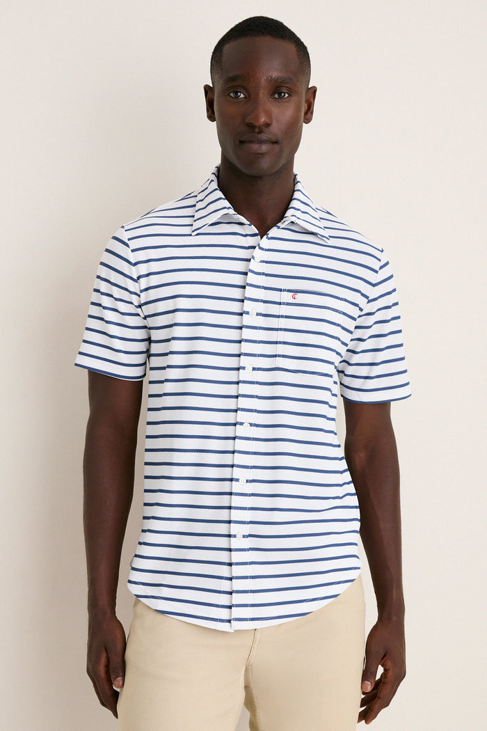 Man wearing the classic White Performance Pique Knit Button Down with blue stripes, featuring a spread collar and chest flap pocket, paired with light-beige trousers for an effortless, high-end look.