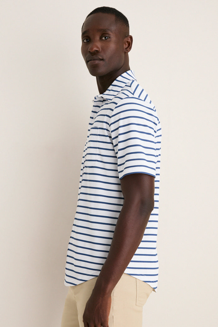 Young man in profile wearing the classic White Performance Pique Knit Button Down with navy stripes and khakis, embodying effortless, high-end style for fun, warm days.