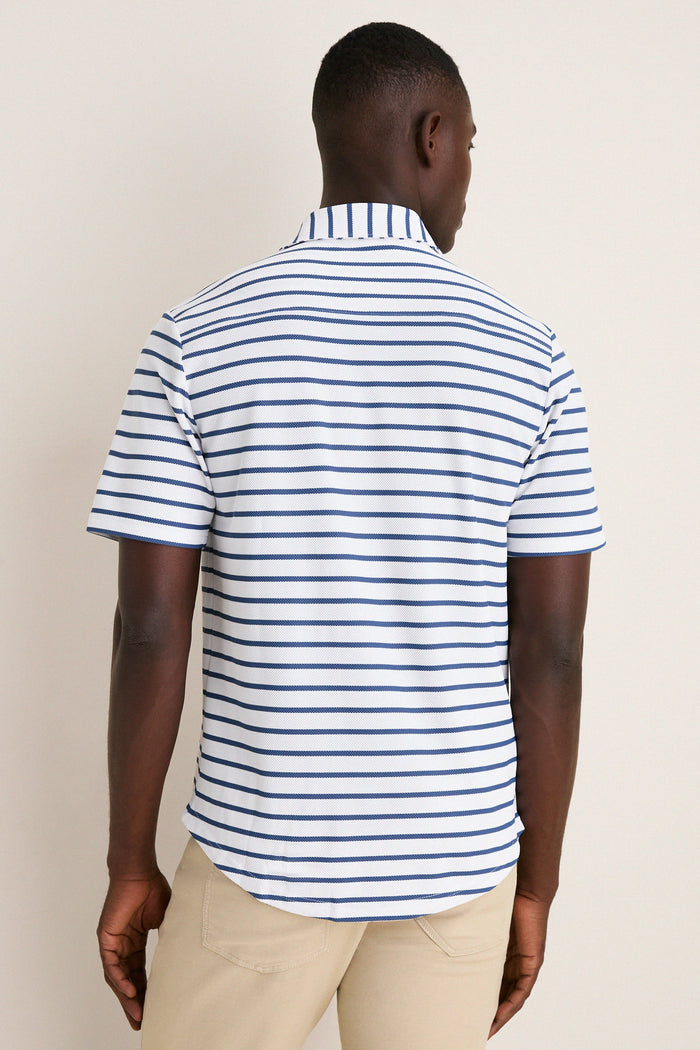 Model in a classic White Performance Pique Knit Button Down, featuring effortless navy-blue stripes and light-beige pants, embodying a high-end, fun style.