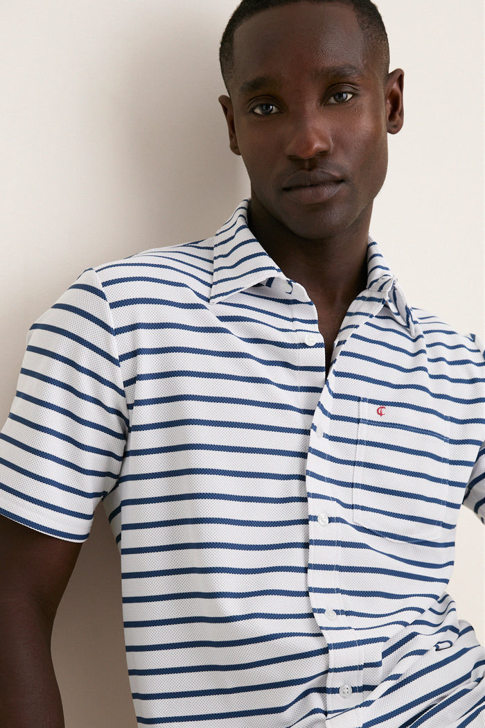 Young man wearing the White Performance Pique Knit Button Down, showcasing its classic, effortless style with navy stripes, flap pocket, and spread collar. Perfect for high-end, fun adventures.