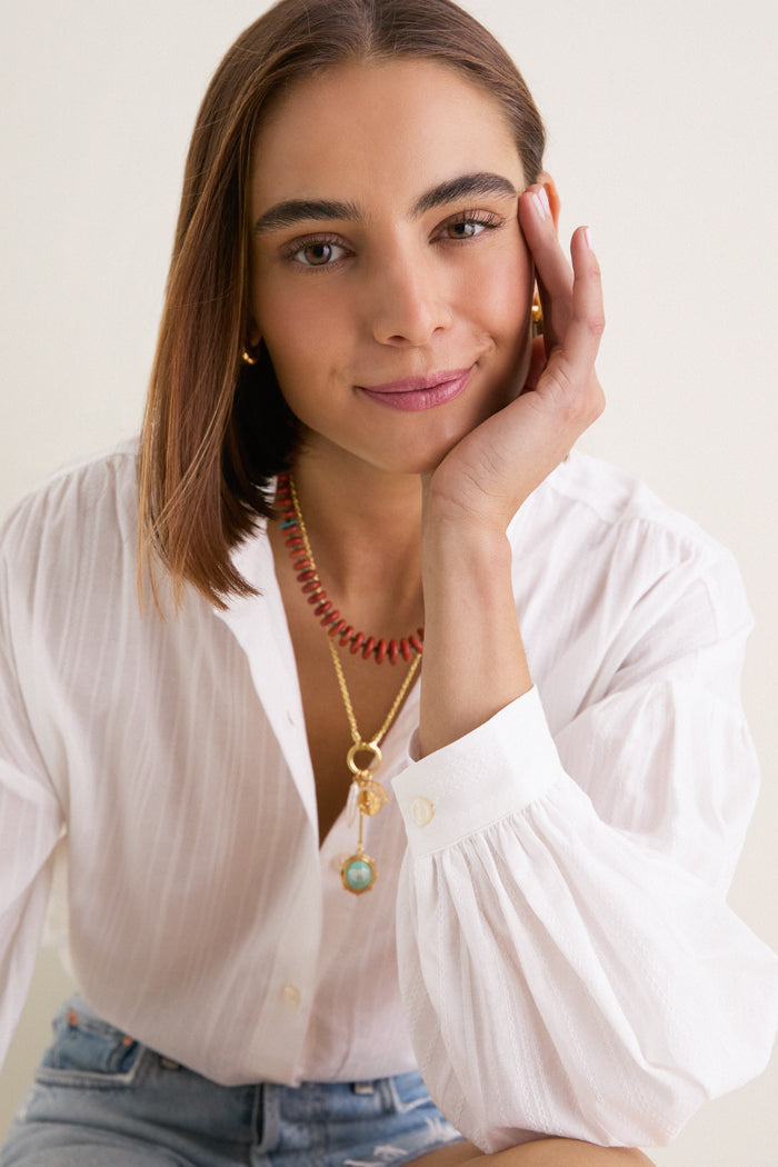 Young woman wearing a classic White Shadow Stripe Juliette Button Down with billowy sleeves and effortless stripes, exuding a fun, high-end style paired with delicate necklaces.