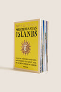 Hardcover book titled Wine & Travel Mediterranean Islands by Assouline, featuring a classic sun-face motif, promises an effortless, fun journey through high-end Mediterranean wine culture.
