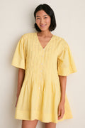 Young woman wearing the classic Yellow Alberte Solid Mini Dress; an effortless, high-end design with pintuck details and buttons, embodying fun, carefree style.