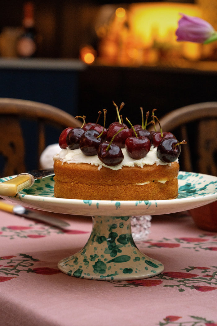 Yellow and Verde Splatter Cake Stand elegantly displays a sponge cake with cherries, embodying a classic and effortless high-end style, perfect for fun entertaining.