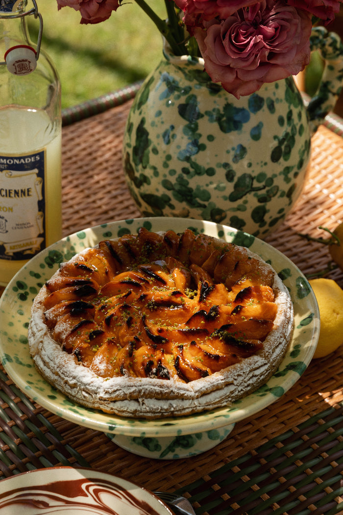 Classic Yellow and Verde Splatter Cake Stand holds a glazed fruit tart, surrounded by lemonade and roses, embodying effortless, fun, high-end entertaining. Perfect for showcasing treats.