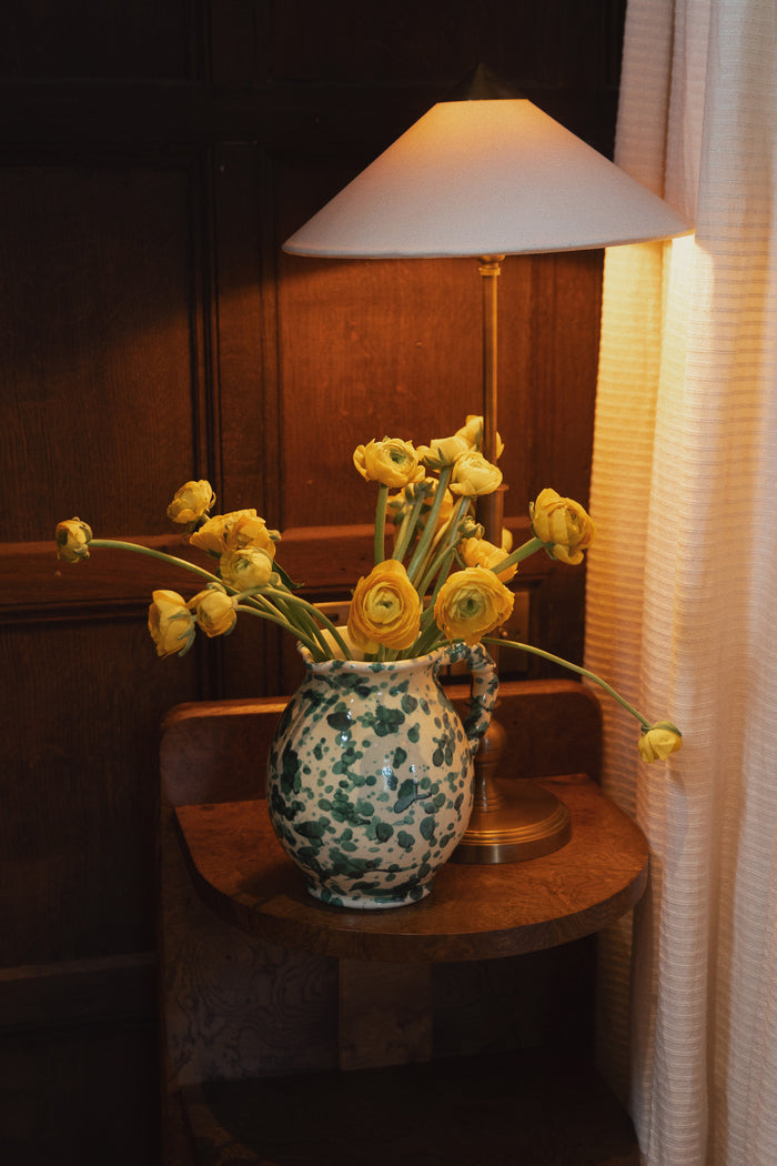 Yellow and Verde Splatter Cigno Jug, classic and handmade in Italy, effortlessly adorns a side table with vibrant blooms, adding a fun, high-end touch.