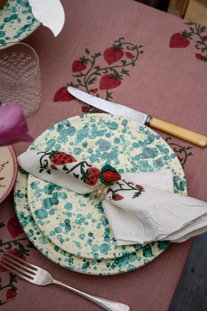 Classic and effortless, the Yellow and Verde Splatter Dinner Plate showcases a fun teal-green bubble glaze, perfect for high-end entertaining with a vibrant strawberry-themed setting.