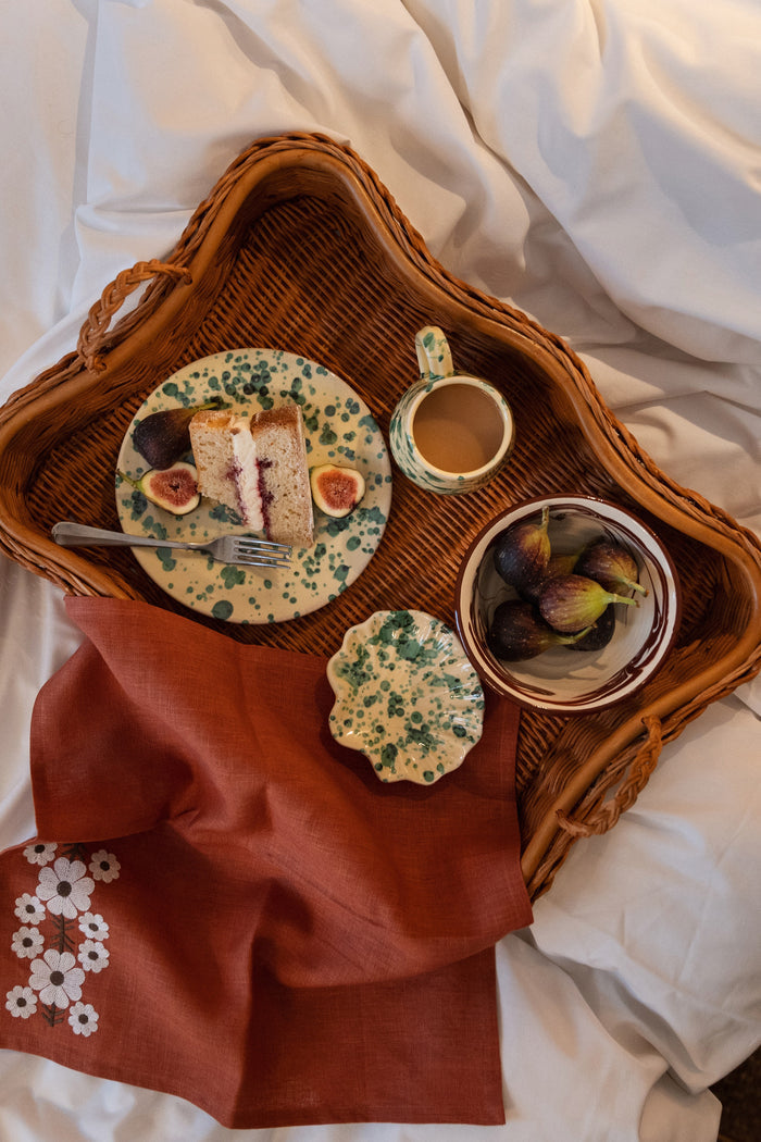 Woven tray on white sheets with a classic Yellow and Verde Splatter Side Plate featuring cake and figs, embodying effortless, high-end elegance for fun dining experiences.