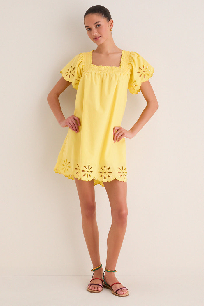 Young woman in a classic, effortless Yellow Floral Eyelet Daisy Mini Dress with puffed sleeves and eyelet details, paired with fun, multi-colored sandals.